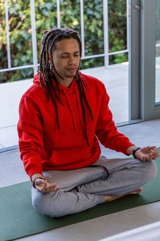 African american man meditating in red hoodie on balcony yoga mat for calm and focus