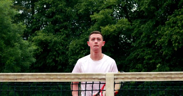 Young man playing tennis outdoors appears focused and ready for the game. Suitable for use in sports-related publications, fitness advertisements, and content promoting outdoor activity.