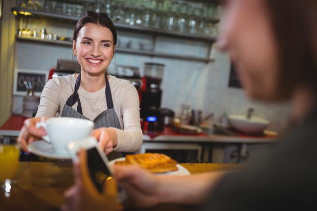 Waitress serving a cup of coffee to customer in cafÃ©