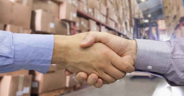 Digital composite of Close-up of business people shaking hands in warehouse
