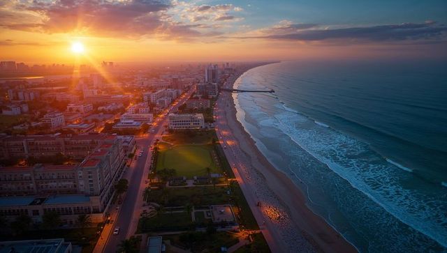 Golden sunset coastline aerial view of urban beachfront with pier, rolling waves, city lights