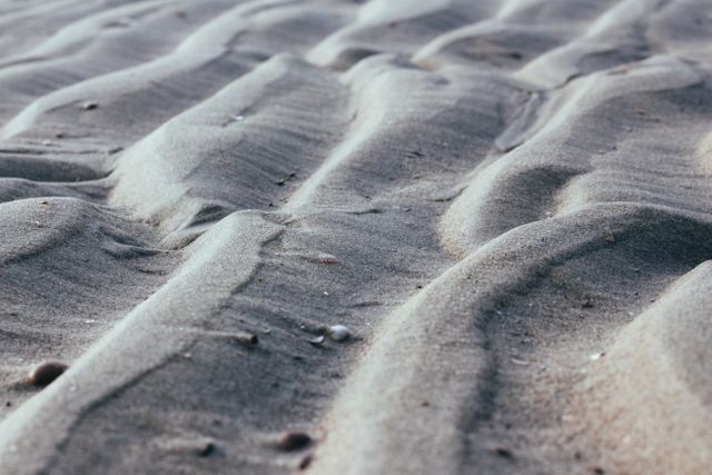 Close-up of soft ripples in sand creating an abstract pattern on beach. Ideal for nature themes, coastal imagery, backgrounds, wallpapers or promotional materials related to outdoor beaches and serenity.