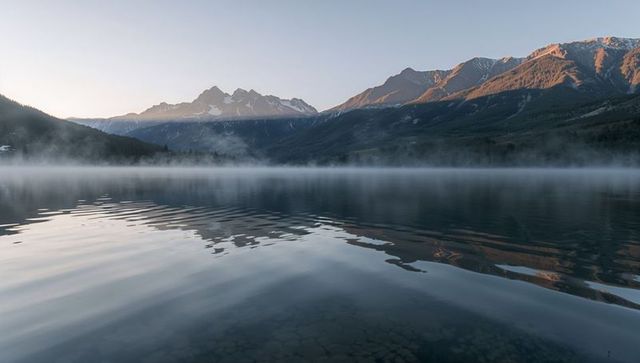 Misty alpine lake at dawn with serene mountain reflections and submerged rocks