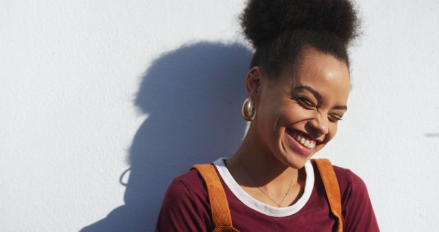 This image of a young woman smiling joyfully against a white background is perfect for use in contexts related to happiness, youth, and positive emotions. Her natural afro hair and casual fashion convey a carefree and trendy vibe, making it suitable for advertisements, social media posts, and lifestyle blogs aiming for an uplifting and relatable atmosphere.