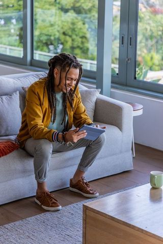 Man sitting on sofa using tablet in bright living room wearing mustard jacket