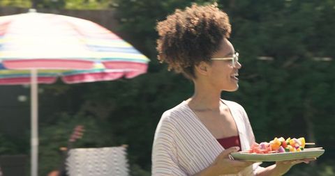 Smiling african american woman carrying fruit skewers outdoors