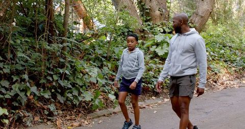 African american father and son walking together on shaded forest trail wearing gray hoodies
