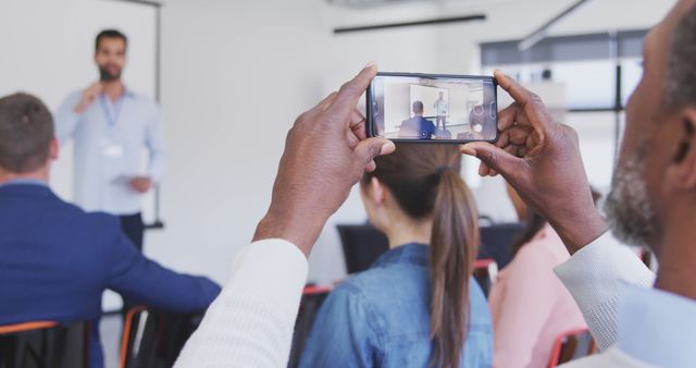Audience member taking a photo with a smartphone while a professional speaks to a business audience. Ideal for corporate training promotions, event marketing, business seminars, technology use in professional contexts, and learning environment visuals.