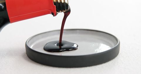 Thick dark liquid pouring from red bottle into dish