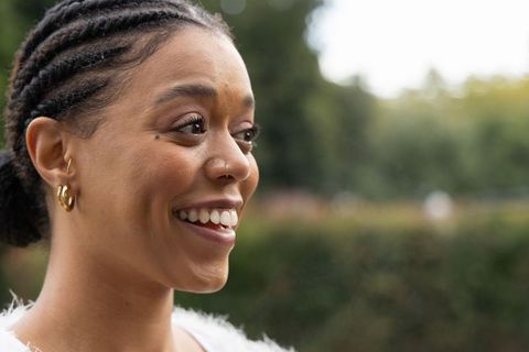 African american woman smiling with cornrows, gold hoops and nose stud in garden