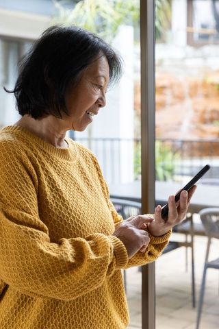Senior Asian Woman Enjoying Smartphone Use in Home near Garden Patio