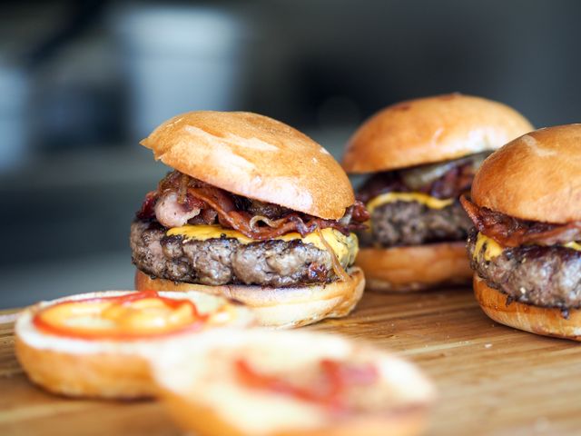 Juicy, grilled beef burgers with melted cheese and crispy bacon, served on a wooden board. Perfect for use in food blogs, restaurant advertisements, menu designs, and social media promotion of culinary delights. Represents mouth-watering American cuisine and home-cooked gourmet meals.