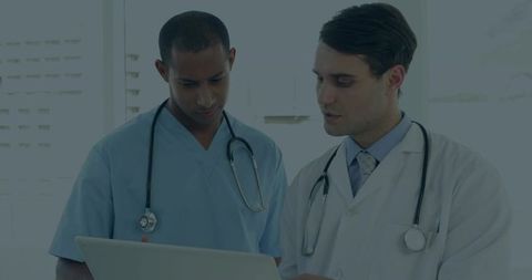 Medical professionals collaborating over laptop in clinic reviewing digital patient records