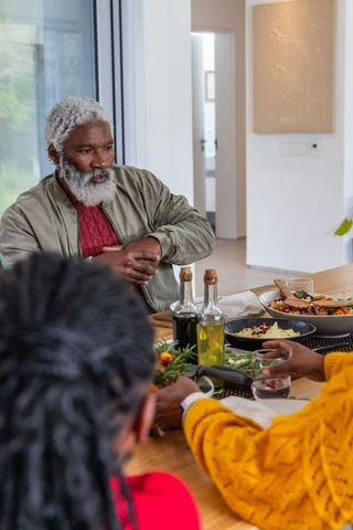 African american family sharing dinner with gray-haired elder leading conversation