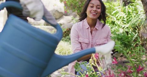Smiling woman gardening with blue watering can in blooming garden