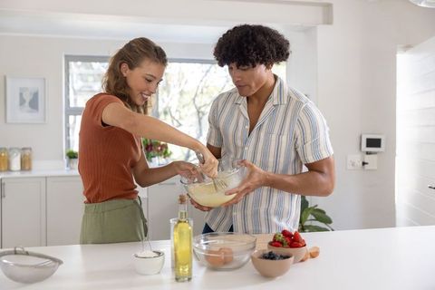 Couple baking together in bright kitchen mixing batter at island with fresh berries