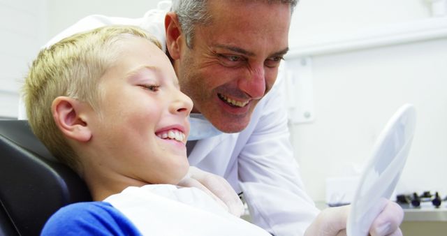 Young boy sitting in dental chair smiling with dentist, celebrating successful dental checkup. Dentist holding mirror, both expressing satisfaction and joy. Commonly used in advertisements for dental clinics, posters about dental hygiene, and educational materials about kids' dental health.