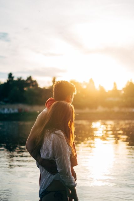 Couple stands by lake during sunset, creating a romantic atmosphere. Use for romantic themes, outdoor activities, relationship content, travel blogs, or serene nature scenes.