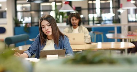 Young professionals studying and working in coworking cafe using tablets and laptops