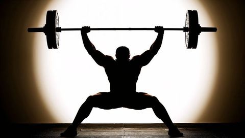 Silhouetted powerlifter lifting overhead barbell in wide squat pose with halo backlight