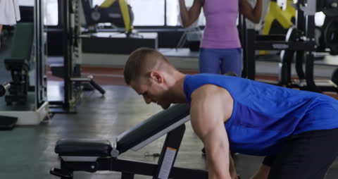Man Lifting Weights in Gym with Workout Partners in Background