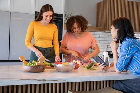 Diverse friends preparing fresh veggie salad together in modern kitchen
