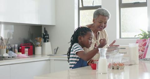 African american grandmother guiding granddaughter mixing batter on kitchen island