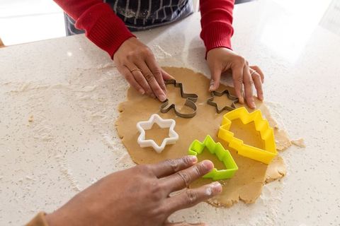 Diverse friends cutting festive cookie dough on sunlit kitchen counter for holiday baking