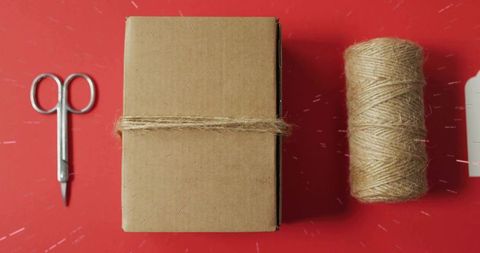 Crafting rustic gift box wrapped with jute twine on red flatlay for handmade packaging