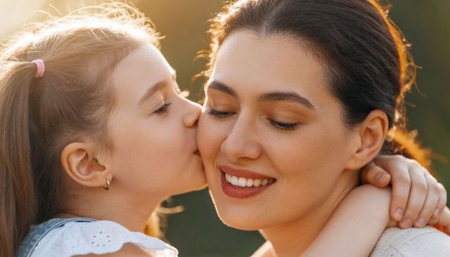 Mother and daughter sharing tender kiss and warm embrace in golden hour glow