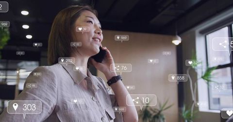 Asian woman speaking on mobile in modern coworking space holding phone wearing smartwatch