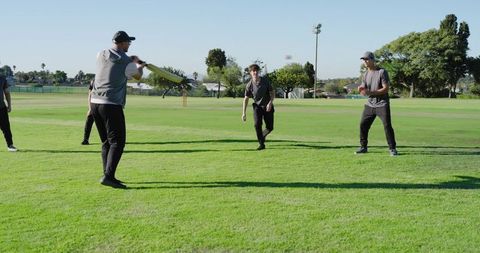 Batsman swinging during casual cricket practice on sunny park field with teammates
