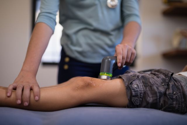 Therapist performing ultrasound scan on boy's knee, focusing on medical treatment and rehabilitation. Useful for illustrating healthcare services, pediatric care, medical diagnostics, and physical therapy. Ideal for use in medical articles, healthcare brochures, and educational materials about child health and recovery.