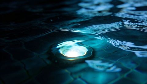Underwater pool light casting rippling caustic patterns over turquoise mosaic tiles