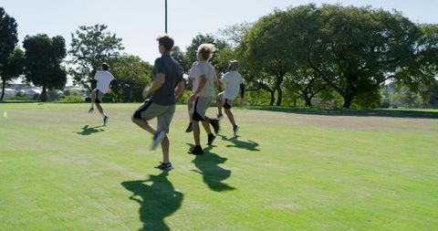 Male teammates training on sunlit grass performing dynamic warm up drills for team fitness