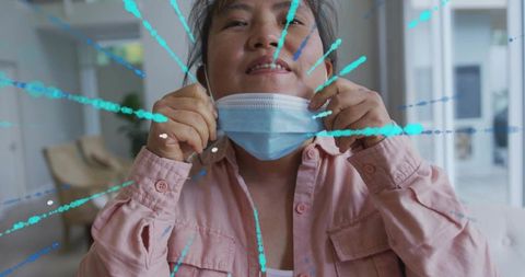 Pulling surgical mask beneath chin smiling korean man removing mask in sunlit lobby