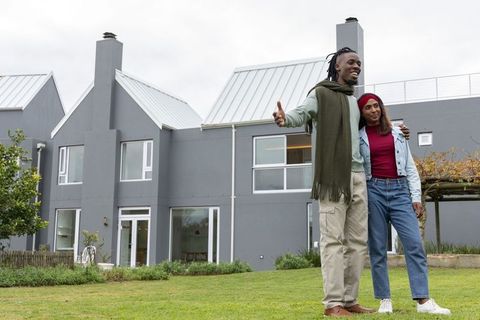 Diverse couple touring modern suburban home standing on lawn with garden and pergola view