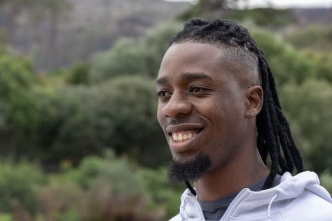 Confident african american man smiling outdoors with dreads and goatee, casual hoodie