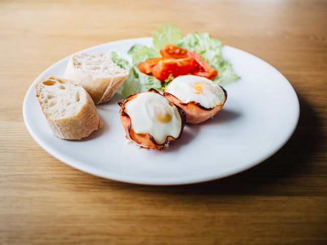 White plate holding a well-balanced breakfast of baked egg cups embedded in ham, fresh lettuce, sliced tomatoes, and sliced bread. Suitable for promoting a healthy breakfast or brunch spread, food blogs, nutrition articles, and restaurant menus.