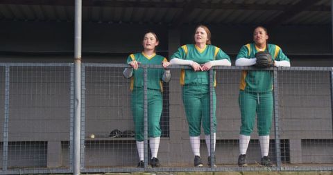 Diverse female softball players watching competitive game from dugout