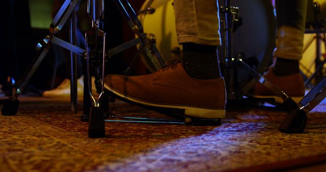 This image showcases a musician's foot pedaling a drum kit during a live performance, illuminated by stage lighting. Ideal for use in promotional material for music events, websites dedicated to musical instruments, or articles about live music and its energetic atmosphere.