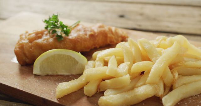 Golden fried fish served with crispy French fries on a wooden board. Garnished with a slice of lemon and parsley. Perfect for illustrating British cuisine, comfort food, seafood dishes, and casual dining. Ideal for use in food blogs, restaurant menus, and culinary websites.