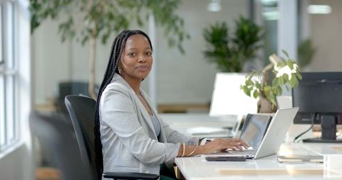 African American businesswoman typing on laptop in bright modern open-plan office with plants
