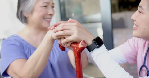 Senior woman receiving support from caregiver with walking cane