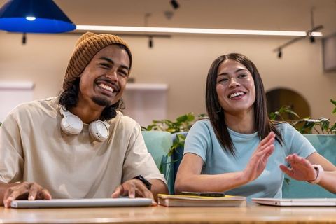 Smiling diverse coworkers collaborating at communal table in modern coworking lounge