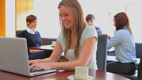 Smiling Student Typing Laptop at Campus Cafeteria