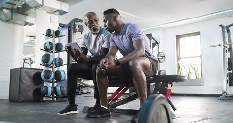 Fitness Trainer Guiding Client with Tablet in Gym