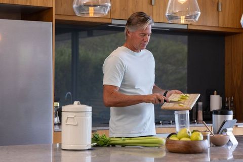 Senior man preparing green smoothie with apples and celery in modern kitchen