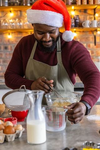African american man in santa hat whisking festive batter for holiday baking in cozy kitchen