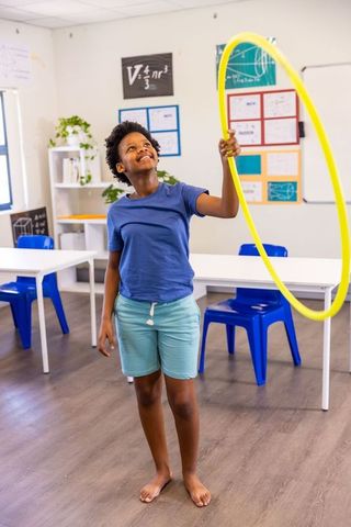 African american child playing with yellow hula hoop in classroom smiling and learning